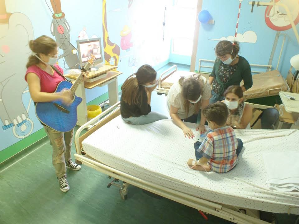 A volunteer playing guitar for a child patient during an art-based circle at a hospital